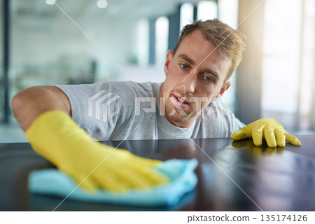 Man with gloves, office cleaning service and janitor dusting dirt for health and hygiene in workplace. Professional cleaner wiping table in workspace, maintenance and disinfectant on cloth for germs. 135174126
