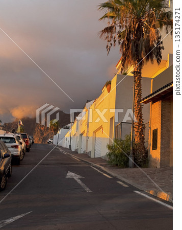 Warm evening sunlight reflecting on colorful building walls and palm trees along a quiet street in Tenerife. 135174271