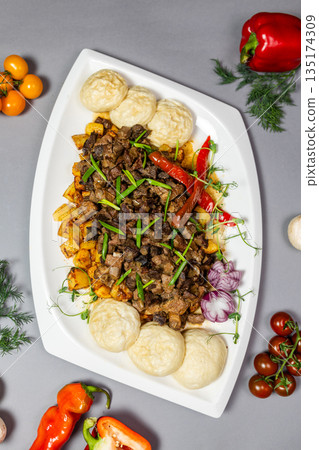 Traditional Kazakh kuyrdak made of fried meat and potatoes, served with dough balls and vegetables. Traditional Kazakh kuyrdak made of fried meat and potatoes, served with dough balls and vegetables. 135174309