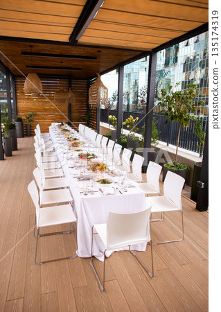 Wide shot of long set table on terrace, elegant table setting for event Wide shot of long set table on terrace, elegant table setting for event 135174319