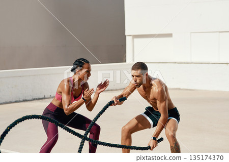 Woman, personal trainer and battle rope training for workout, exercise or fitness outdoors. Fit, active or serious coaching with man person exercising with ropes for sports endurance or motivation Woman, personal trainer and battle rope training for workout, exercise or fitness outdoors. Fit, active or serious coaching with man person exercising with ropes for sports endurance or motivation 135174370