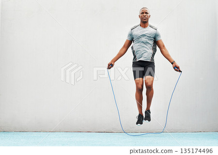 Jump, rope and training with black man skipping in stadium for sports, workout practice and cardio. Health and body with athlete jumping on track for strong, mockup space and exercise against wall Jump, rope and training with black man skipping in stadium for sports, workout practice and cardio. Health and body with athlete jumping on track for strong, mockup space and exercise against wall 135174496