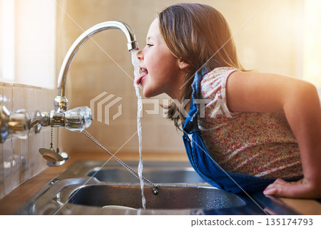 Drinking water, tap and child with tongue out in a home kitchen with a smile. House, kids and youth feeling thirsty, cheeky and curious at a sink trying to drink from faucet for hydration alone Drinking water, tap and child with tongue out in a home kitchen with a smile. House, kids and youth feeling thirsty, cheeky and curious at a sink trying to drink from faucet for hydration alone 135174793