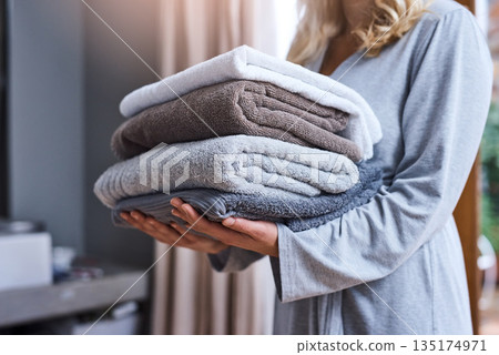 Laundry, cleaning and a woman with a stack of towels in her home for hygiene or a spring clean day. Housework, housewife and a female person carrying a pile of fresh or soft fabric in a living room 135174971