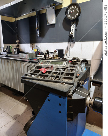 A machine is center stage in an automotive workshop with tools scattered on the counter. A clock on the wall shows the time in the busy repair space A machine is center stage in an automotive workshop with tools scattered on the counter. A clock on the wall shows the time in the busy repair space 135175492