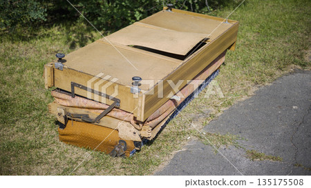 A wooden cart rests on the grass close to a path in a green area. The cart shows signs of wear, with some parts missing or damaged in the sunlight A wooden cart rests on the grass close to a path in a green area. The cart shows signs of wear, with some parts missing or damaged in the sunlight 135175508
