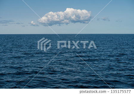 Blue ocean under a clear sky with a single cloud drifting calmly overhead Blue ocean under a clear sky with a single cloud drifting calmly overhead 135175577