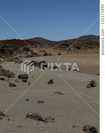 Curved terrain of sand and volcanic rock formations with distant hills under strong sunlight in Teide National Park. Curved terrain of sand and volcanic rock formations with distant hills under strong sunlight in Teide National Park. 135175946