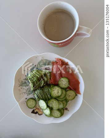 Top-down view of a nutritious breakfast bowl with cucumbers, salmon, avocado and coffee on a clean white surface. 135176004