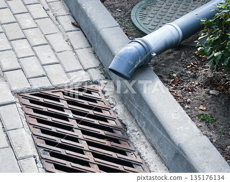 Street drain and pipe on a paved sidewalk with manhole cover. 135176134