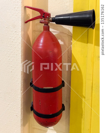 Wall-mounted red fire extinguisher on a yellow wall. Wall-mounted red fire extinguisher on a yellow wall. 135176162