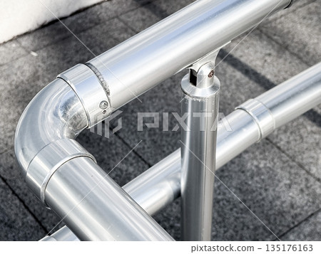 Metal pipe railing on a gray tiled surface in sunlight. Metal pipe railing on a gray tiled surface in sunlight. 135176163
