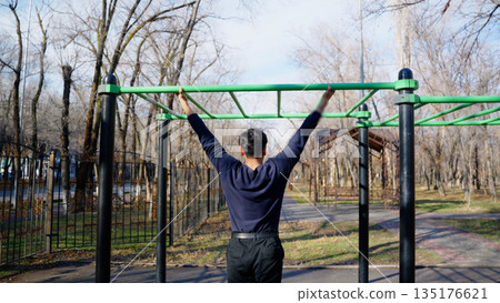 Man exercising on pull up bar outdoors Man exercising on pull up bar outdoors 135176621