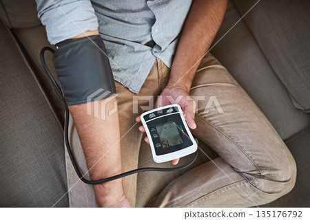 Hypertension, closeup and person with home test for blood pressure on living room sofa for medical or health exam. Monitor, reading and man with equipment for chronic disease or stress from top view Hypertension, closeup and person with home test for blood pressure on living room sofa for medical or health exam. Monitor, reading and man with equipment for chronic disease or stress from top view 135176792