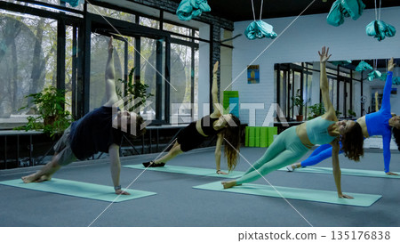 Group of people doing plank yoga pose in a studio Group of people doing plank yoga pose in a studio 135176838