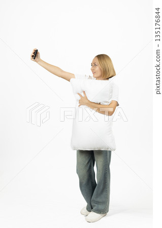 Young woman in a white sweatshirt holding a pillow Young woman in a white sweatshirt holding a pillow 135176844