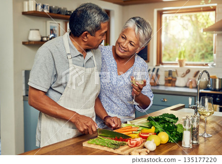 Old couple in kitchen, wine and happiness, cooking healthy food together in home with vegetables. Drink, smile and senior woman with glass in house with man, meal prep and happy lunch in retirement. 135177220