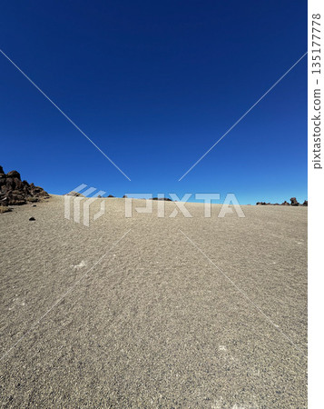 Flat barren volcanic sand landscape with deep blue sky and distant rock formations in Teide National Park, Tenerife. Flat barren volcanic sand landscape with deep blue sky and distant rock formations in Teide National Park, Tenerife. 135177778