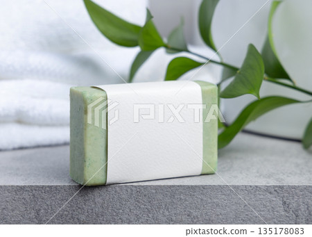 Soap bar with blank label against green leaves and white bath towels on grey stone, mockup Soap bar with blank label against green leaves and white bath towels on grey stone, mockup 135178083