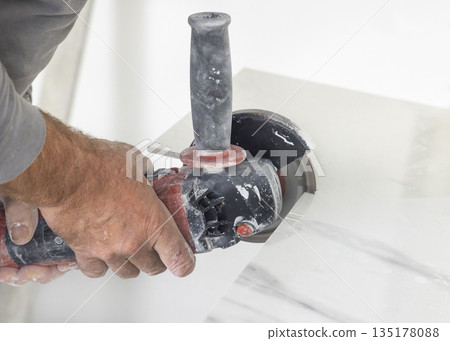 Craftman in grey shirt cuts a gray marble tile using an angle grinder. Hands closeup Craftman in grey shirt cuts a gray marble tile using an angle grinder. Hands closeup 135178088