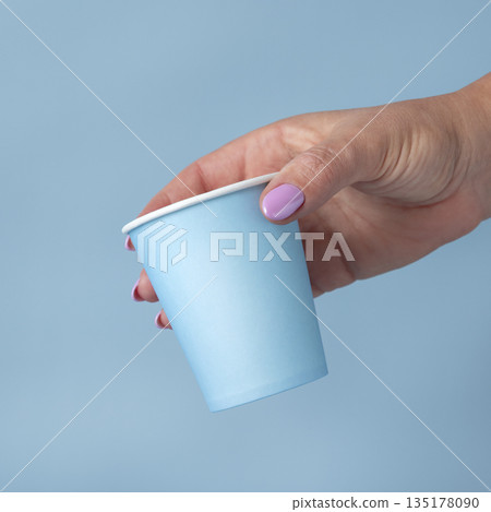 Female hand with disposable light blue paper cup closeup, mockup, copy space. Single-use cup Female hand with disposable light blue paper cup closeup, mockup, copy space. Single-use cup 135178090