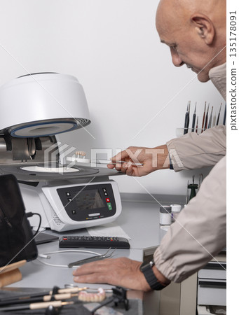 Orthodont men puts tooth implants into dental ceramic oven for baking enamel. Dental prosthetics Orthodont men puts tooth implants into dental ceramic oven for baking enamel. Dental prosthetics 135178091