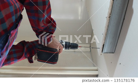 A view from below of a worker holding a screwdriver while fixing paneling to a convex wall in a room, covering and securing the material to a metal profile in an indoor partition structure. 135178176