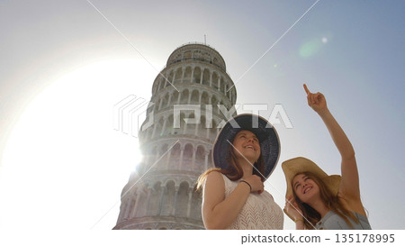 Two attractive women show to each other something under the tower of pisa Two attractive women show to each other something under the tower of pisa 135178995