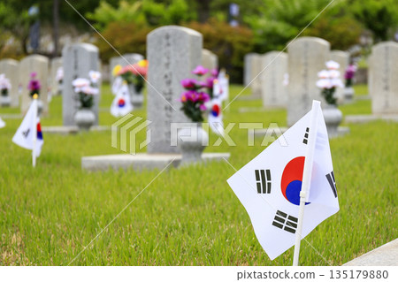 Spring scenery at the Seoul National Cemetery with a tombstone and the Taegeukgi painted on a green lawn. 135179880