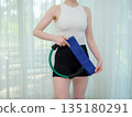 Young woman holding fitness ring and resistance band at home. Concept of home workout, strength training, and healthy lifestyle. Female preparing equipment for online fitness session. 135180291