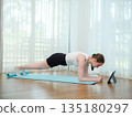 Young woman doing plank exercise at home on yoga mat. Concept of core strength, fitness, and online workout. Female holding plank position while following virtual fitness class on a tablet. 135180297