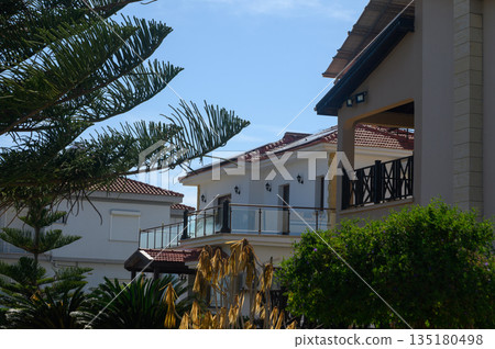 Elegant coastal villa surrounded by lush greenery under a clear blue sky in a sunny seaside location Elegant coastal villa surrounded by lush greenery under a clear blue sky in a sunny seaside location 135180498