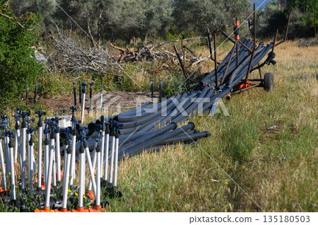 Long rows of irrigation pipes arranged thoughtfully in a lush green field under bright sunlight near olive groves in a rural landscape Long rows of irrigation pipes arranged thoughtfully in a lush green field under bright sunlight near olive groves in a rural landscape 135180503