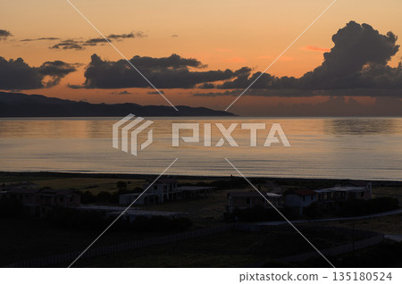 Serene coastal sunset casts golden hues over peaceful waters and quiet homes along the shore 135180524