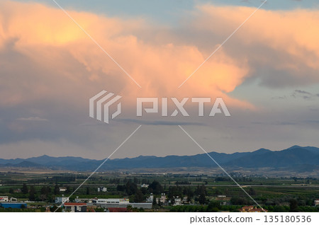 Majestic clouds gracefully billow over serene mountains at dusk, casting soft hues across the tranquil landscape and rural fields Majestic clouds gracefully billow over serene mountains at dusk, casting soft hues across the tranquil landscape and rural fields 135180536