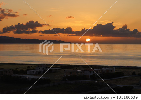 Vibrant sunset casts warm hues over tranquil seaside village along golden shores of a serene evening 135180539