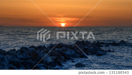 Golden horizon welcomes twilight over tranquil waters, casting silhouettes on rocky shorelines near the coast Golden horizon welcomes twilight over tranquil waters, casting silhouettes on rocky shorelines near the coast 135180543