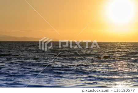 Sunset over the ocean illuminates the sandy beach as people enjoy a relaxing evening stroll Sunset over the ocean illuminates the sandy beach as people enjoy a relaxing evening stroll 135180577