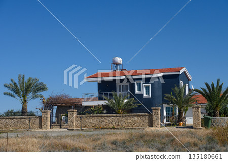 Charming blue house with vibrant palm trees under a clear sky on a serene afternoon in the countryside Charming blue house with vibrant palm trees under a clear sky on a serene afternoon in the countryside 135180661