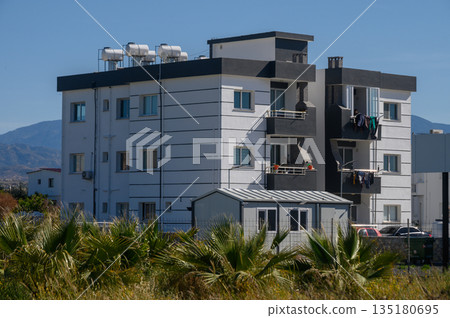 Contemporary apartment building amidst green landscape with mountains in the background during a clear sunny day Contemporary apartment building amidst green landscape with mountains in the background during a clear sunny day 135180695