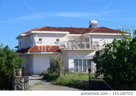 Captivating view of an abandoned villa surrounded by lush greenery on a sunny day in a quiet countryside location 135180703
