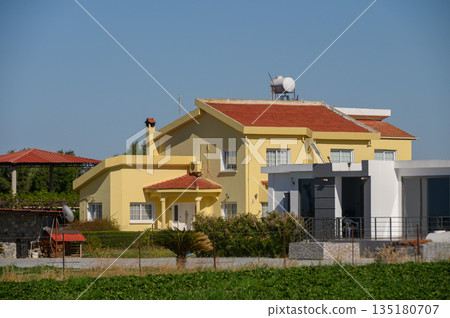 Charming yellow house nestled among fields with clear blue skies and a lovely garden in the background Charming yellow house nestled among fields with clear blue skies and a lovely garden in the background 135180707