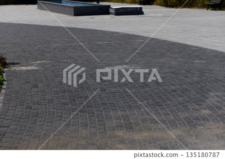 Curved stone pathway leading to a serene water feature in a peaceful outdoor space during bright daylight 135180787