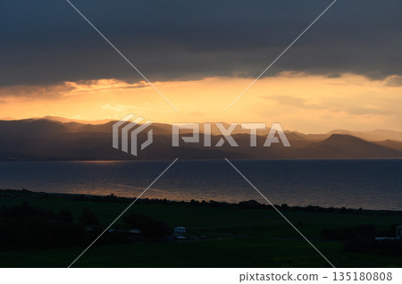 Golden hues illuminate the mountains above a calm sea at sunset in a secluded coastal region Golden hues illuminate the mountains above a calm sea at sunset in a secluded coastal region 135180808