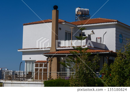 Sunny day at a charming coastal villa with a vibrant garden and terracotta roof under a clear blue sky 135180824