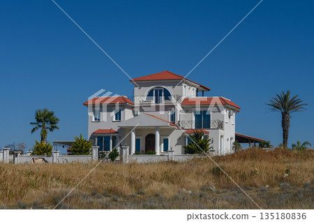 Elegant Mediterranean style villa surrounded by golden grass under a clear blue sky in a tranquil setting 135180836