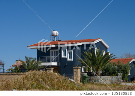 Modern house with a striking design surrounded by lush greenery under a clear blue sky Modern house with a striking design surrounded by lush greenery under a clear blue sky 135180838