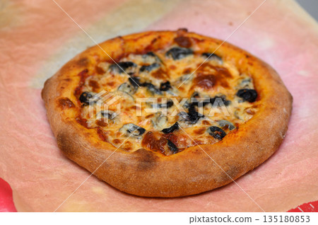 Deliciously golden-brown pizza topped with olives and cheese presented on parchment paper in a cozy kitchen setting 135180853