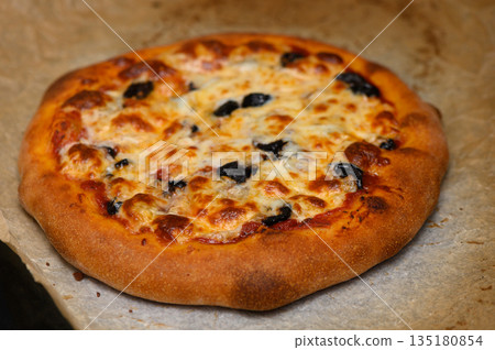 Delicious homemade pizza topped with olives, bubbling cheese, and golden crust, freshly baked in a cozy kitchen Delicious homemade pizza topped with olives, bubbling cheese, and golden crust, freshly baked in a cozy kitchen 135180854