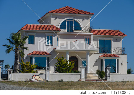 Beautiful modern villa with terracotta roof and sea view in a sunny coastal setting, showcasing elegant architecture and lush greenery Beautiful modern villa with terracotta roof and sea view in a sunny coastal setting, showcasing elegant architecture and lush greenery 135180862